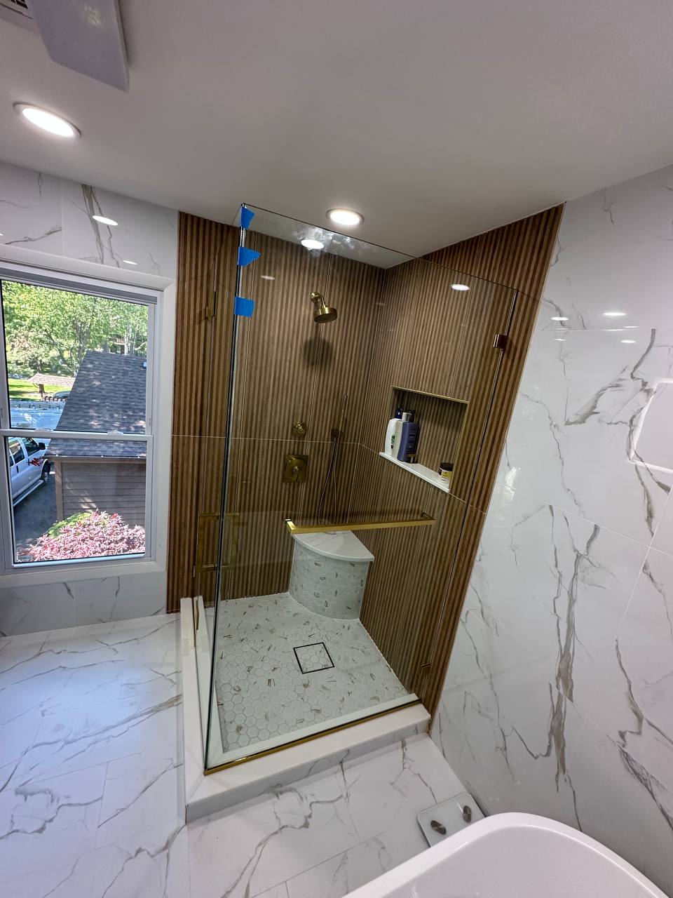Finished clear tempered shower door in an Edison NJ bathroom with brushed brass hardware, warm vertical tile, and white marble-look wall tile.