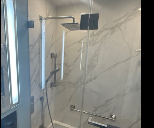 Frameless tub enclosure with chrome hardware against white marble tile — remediated NYC project