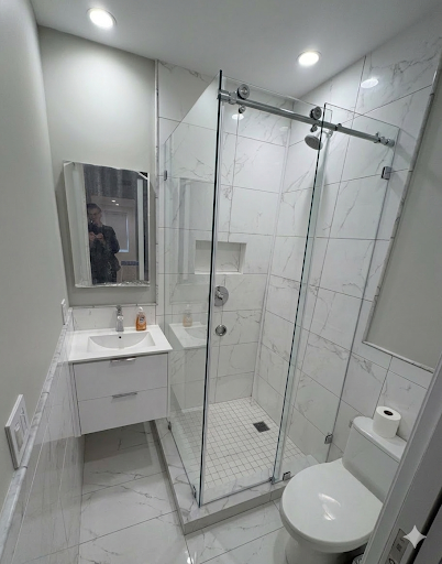 Sliding frameless shower door with top chrome rail in white marble tile compact bathroom NYC