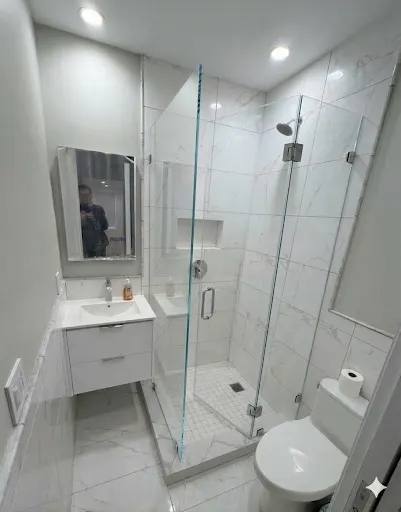 Hinged frameless shower enclosure with fixed panel and chrome hardware in white marble tile bathroom NYC