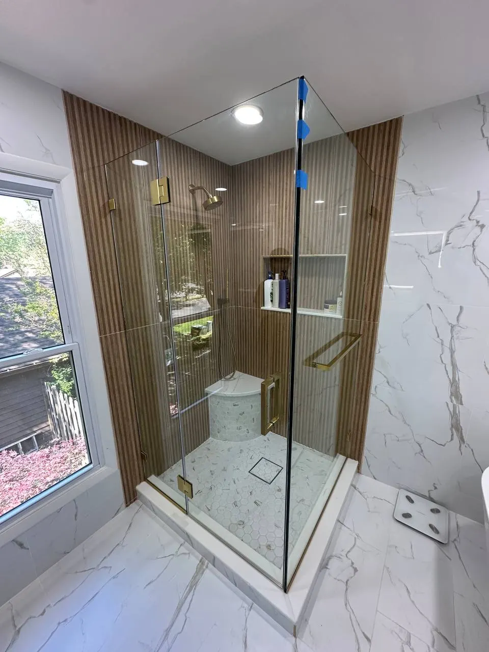 Clear tempered shower door and fixed panel in an Edison NJ bathroom with brushed brass hardware and marble-look tile.
